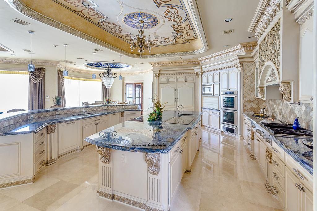 آشپزخانه بزرگ و لوکس با کابینت های کلاسیک سفید، کابینت جزیره ای و سنگ اپن مرمر آبی که سقف آن با گچ ونیزی تزیین شده است